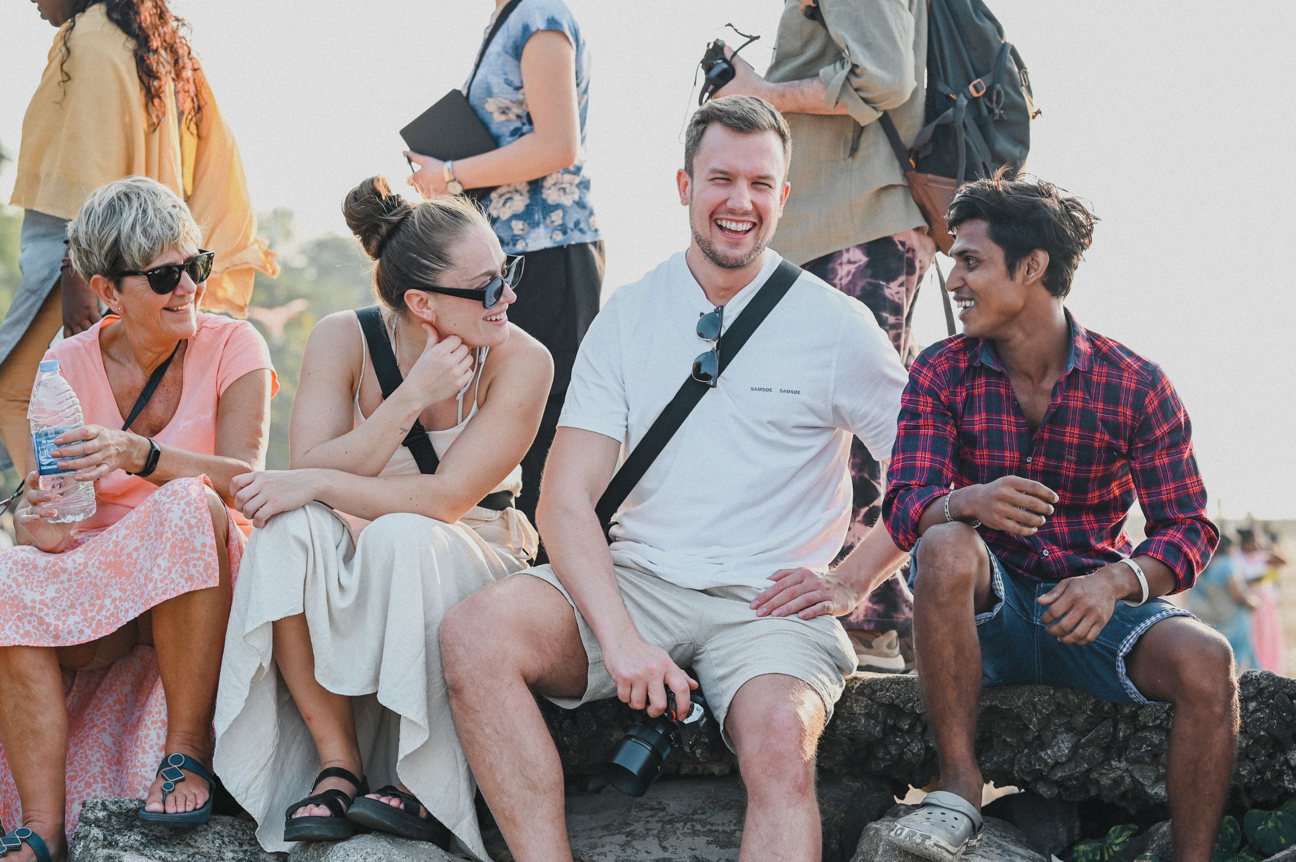 A diverse group of friends laughing and enjoying a sunny day outdoors, captured in candid moment.
