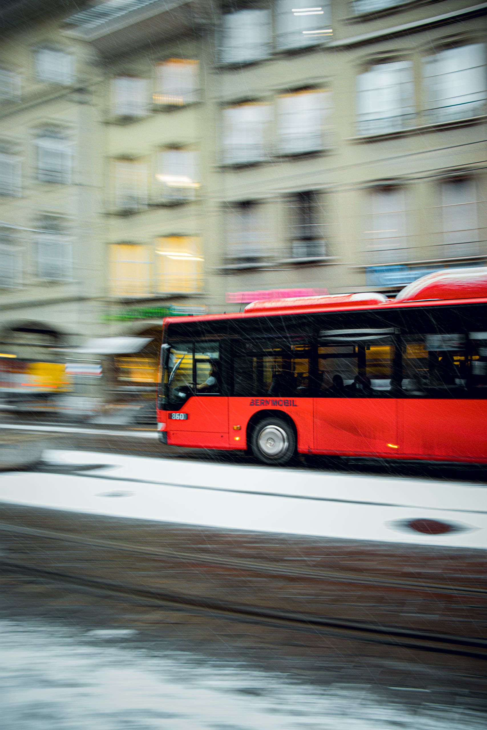 A red bus speeds through a snowy street in Bern, Switzerland, showcasing urban winter commute.